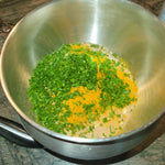 Metal bowl with a mixture of green herbs and yellow spices on a wooden surface